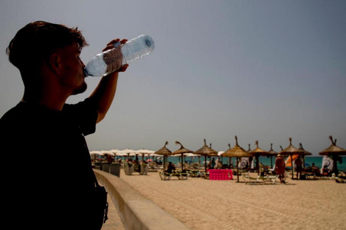 Un chico bebiendo en la playa de una botella de agua de plástico.