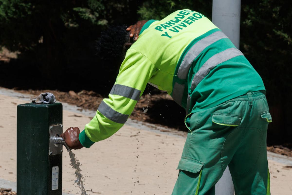 Un trabajador del equipo de Parques y Jardines de Madrid se refresca en una fuente.
