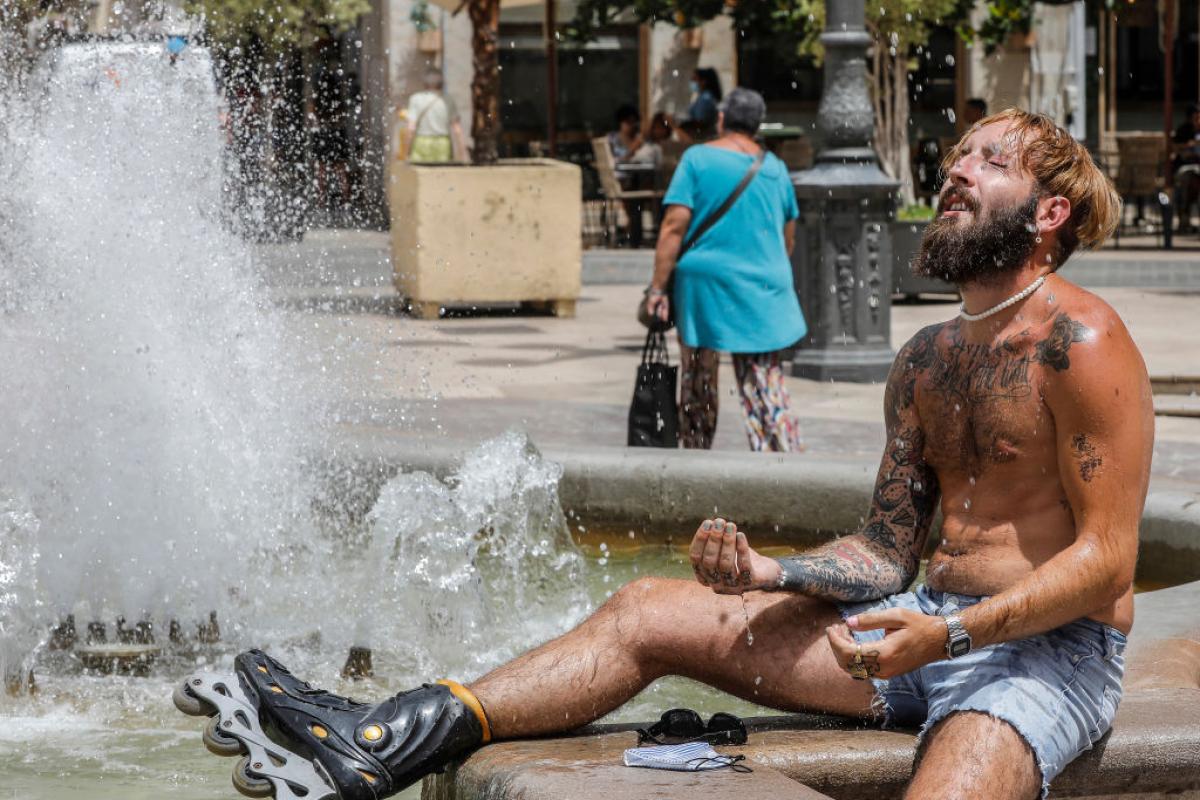 Un hombre se refresca en una fuente, en una fotografía de archivo