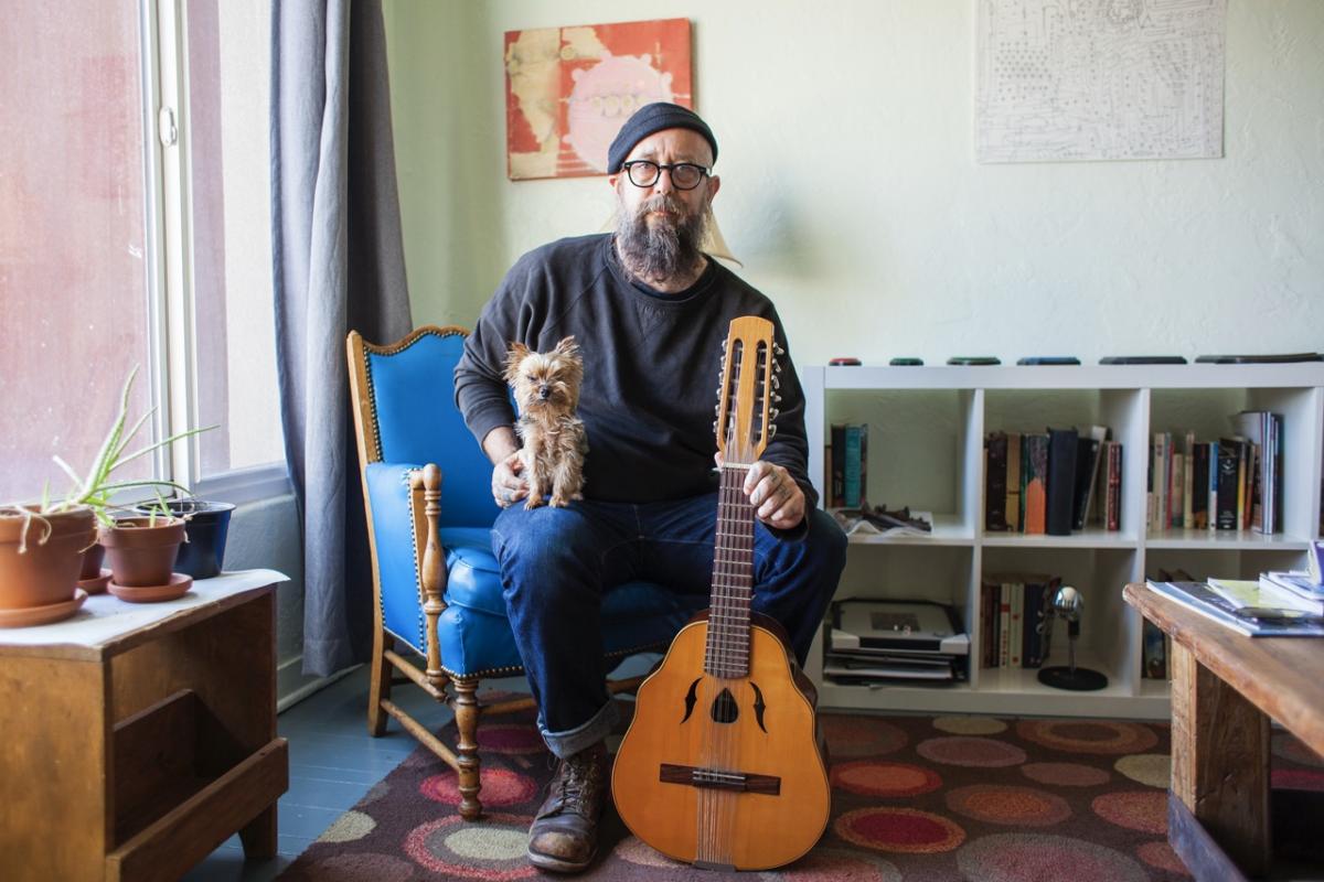 Un hombre posa con su perro y su guitarra en el salón de su casa: autenticidad, estilo y carisma en estado puro.