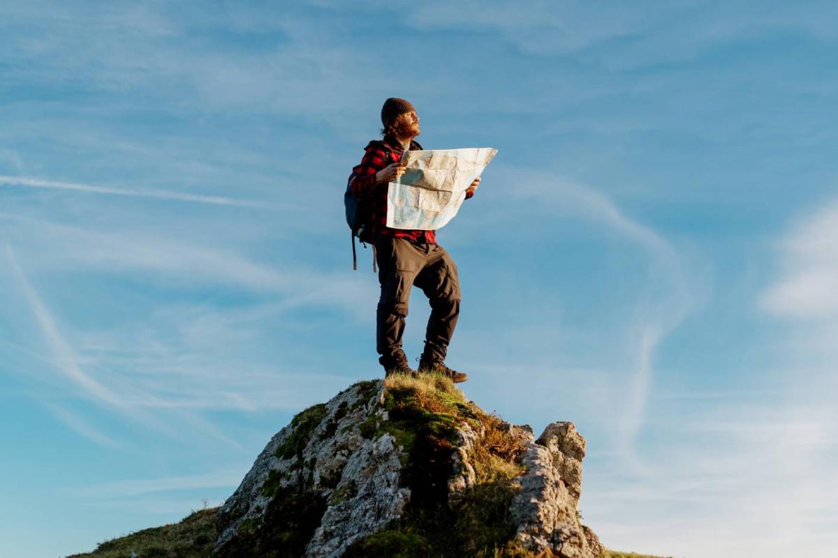 Un hombre perdido contempla el mapa y el horizonte sobre una roca