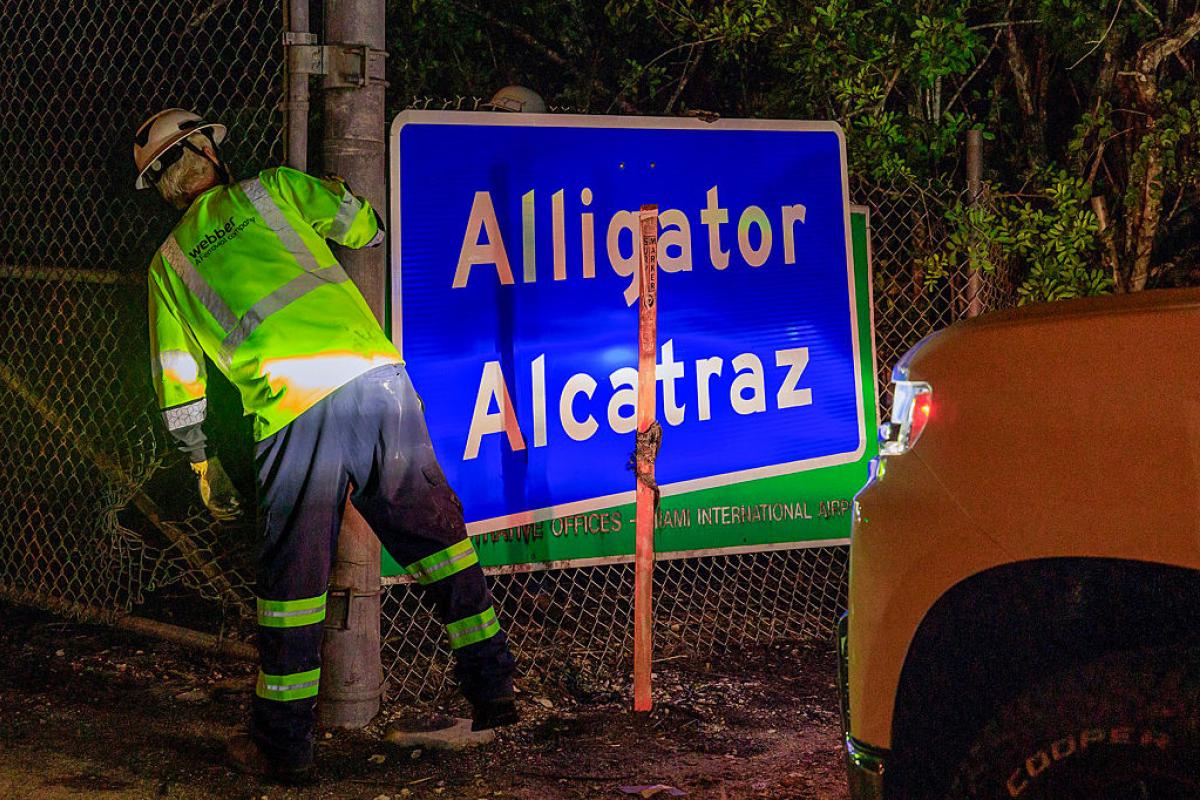 Un operario instalando una señal de 'Alligator Alcatraz'.