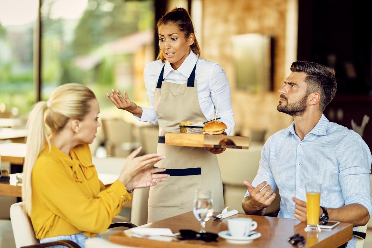 Dos personas discutiendo con la camarera en un restaurante.
