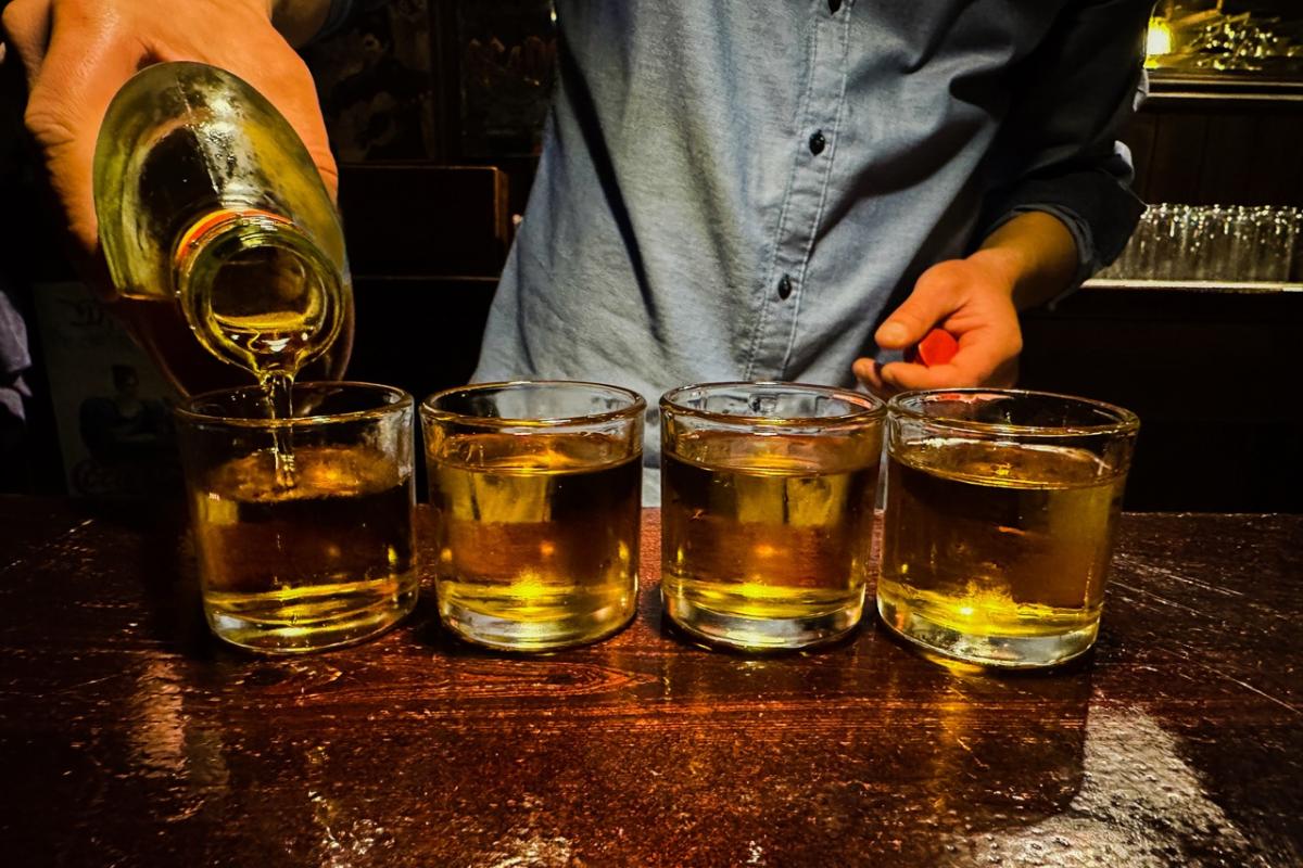 Un camarero sirve varias copas en la barra de un bar.