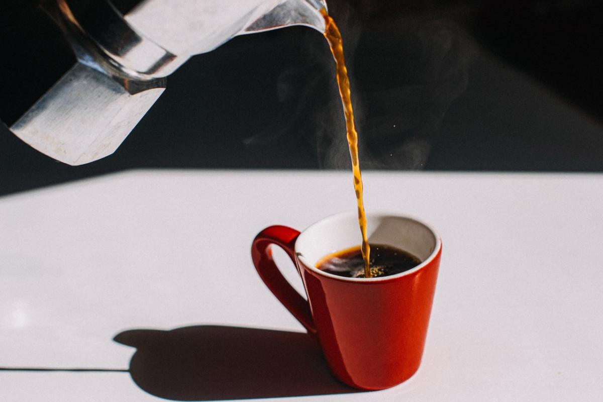 Café servido en taza roja desde cafetera italiana.