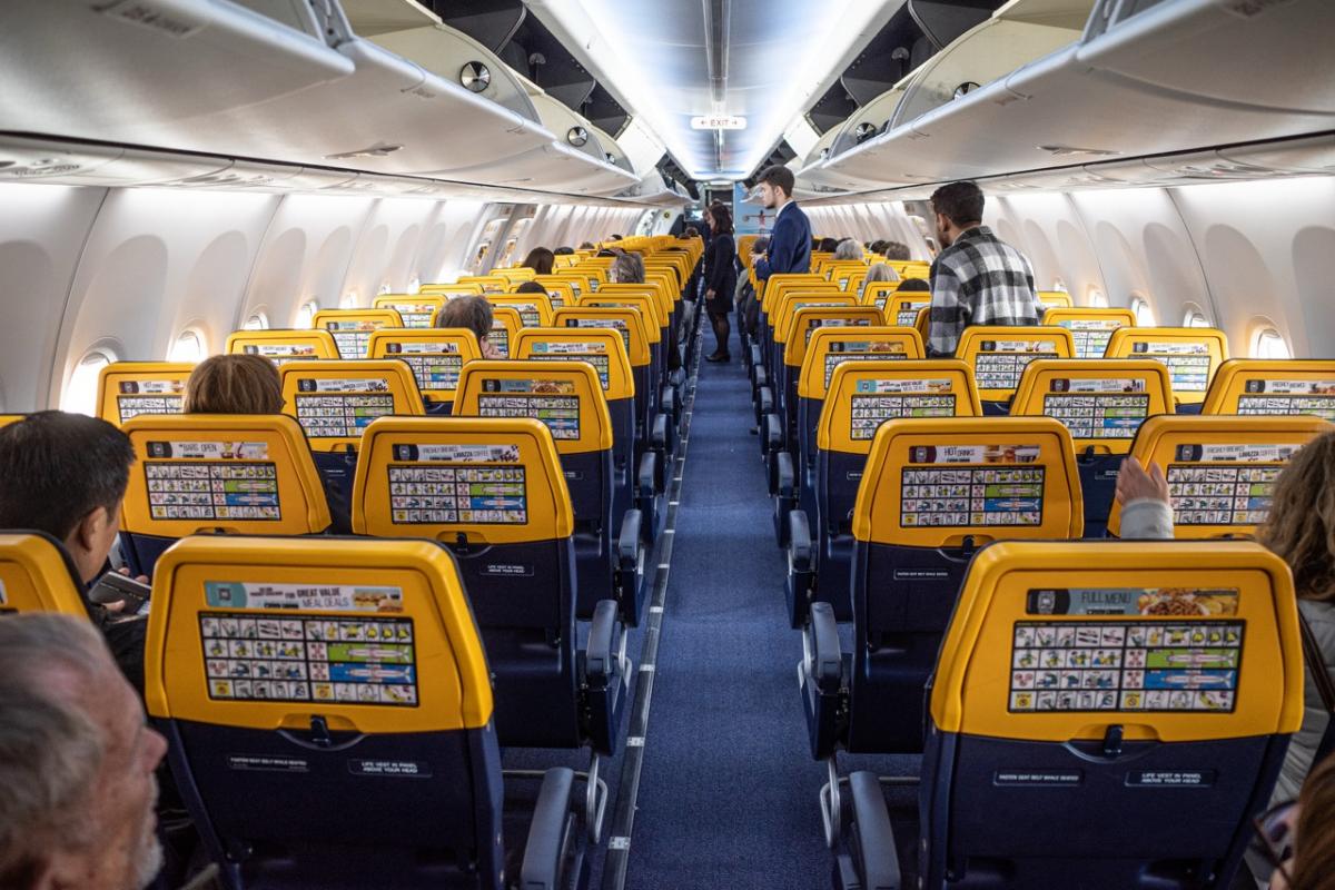 Interior de un avión de Ryanair con pasajeros sentados y tripulación atendiendo en cabina.