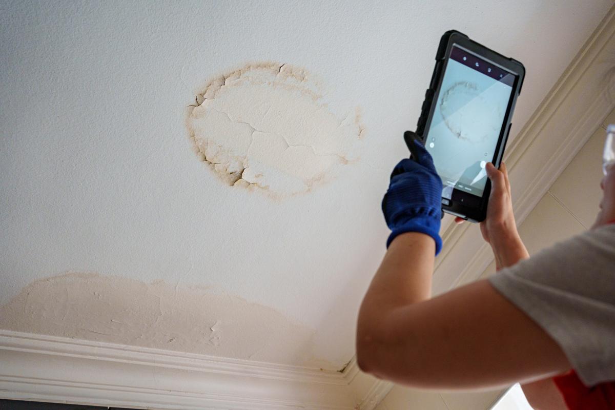 Persona fotografiando con una tableta las manchas de humedad y moho en el techo de una vivienda en la Provenza francesa