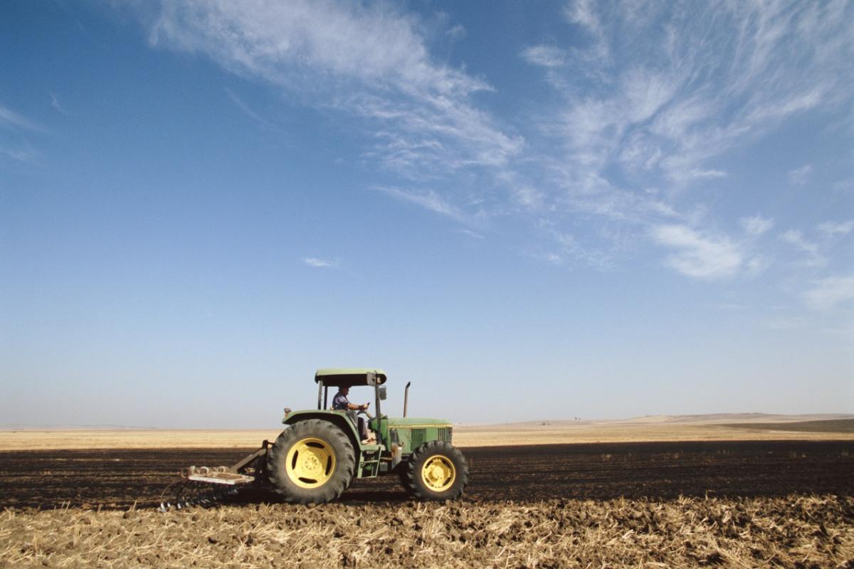 Tractor verde arando un campo bajo un cielo despejado.