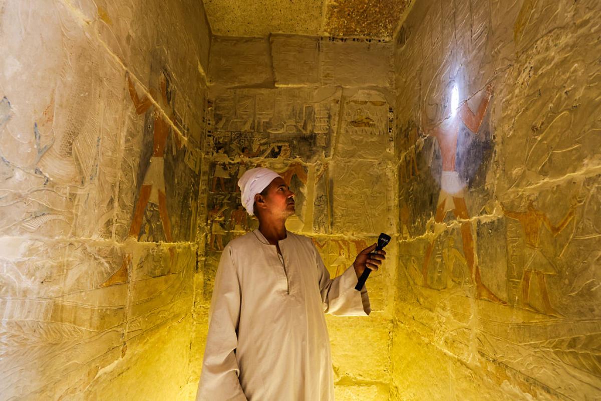 Un guía egipcio ilumina con una linterna los grabados de una tumba del Imperio Antiguo en Saqqara, Egipto.