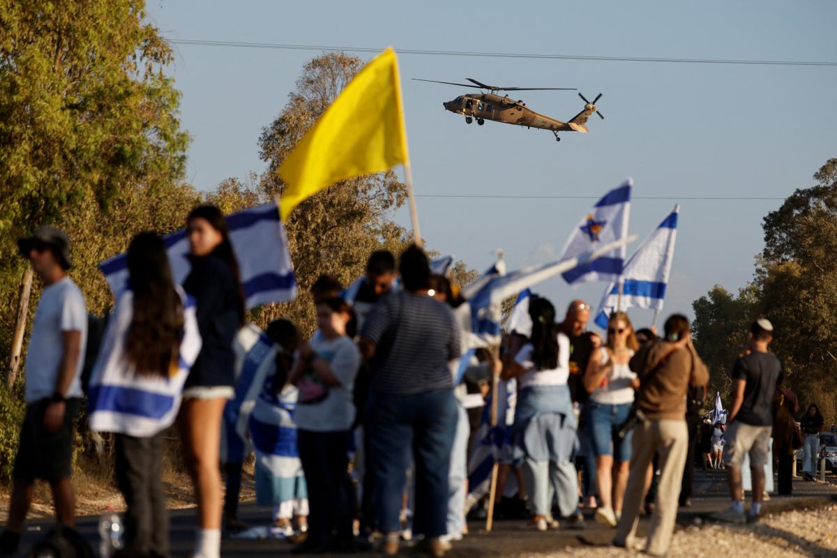 Un helicóptero vuela mientras la gente se reúne, en Reim (Israel), en la base donde se espera que lleguen los rehenes de Israel, este lunes.
