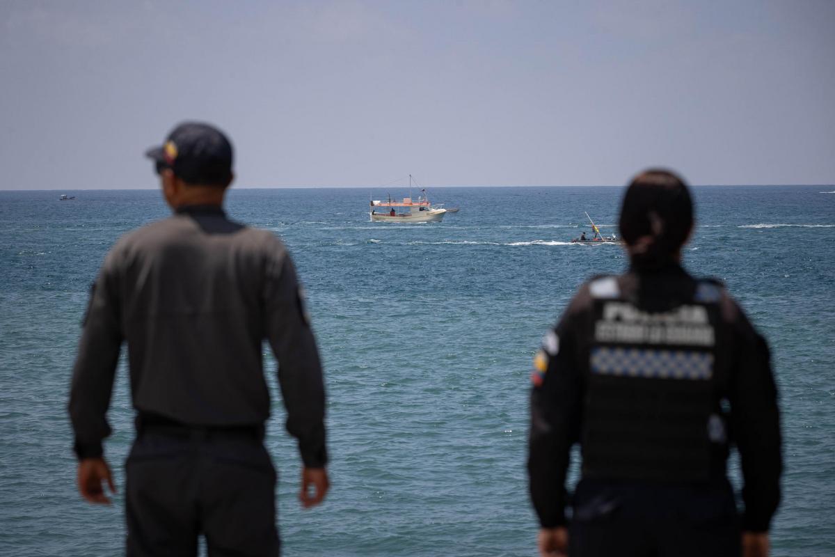 Agentes de la Policía de Venezuela vigilan la costa de La Guaira, con un barco al fondo, en el mar.