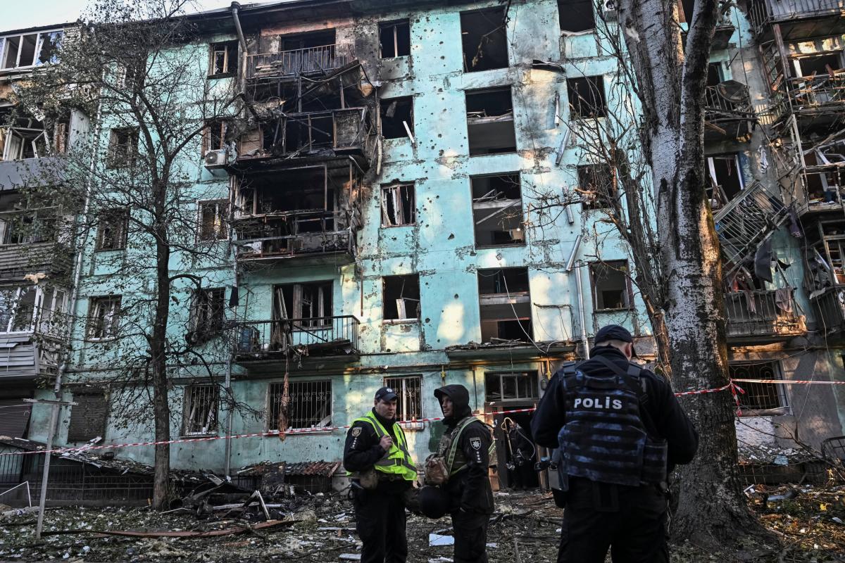 Cráter negro en un edificio residencial de Zaporiyia, atacado por Rusia, mientras agentes de policía montan guardia en los alrededores.