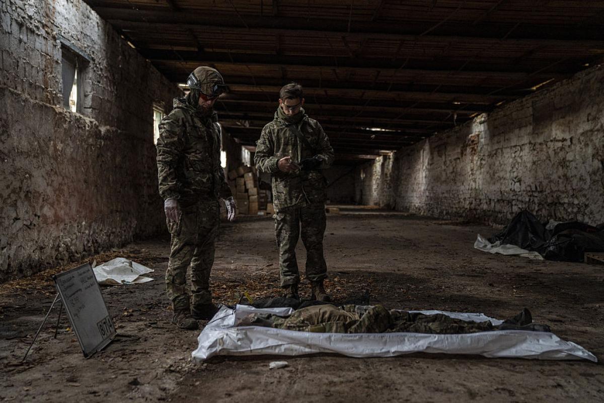 Dos voluntarios con atuendo militar tratan de identificar el cuerpo de un soldado ruso muerto en Ucrania.