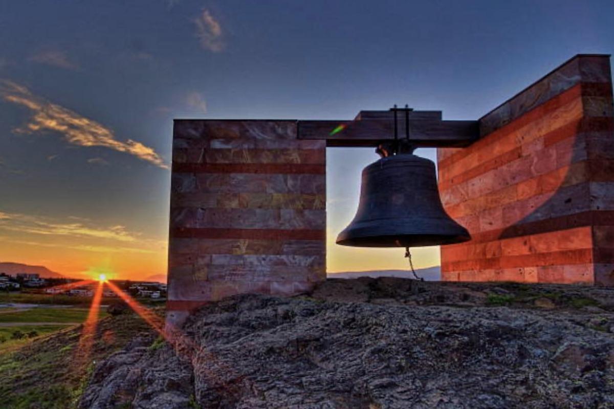 Una campana en medio del campo con un atardecer de fondo