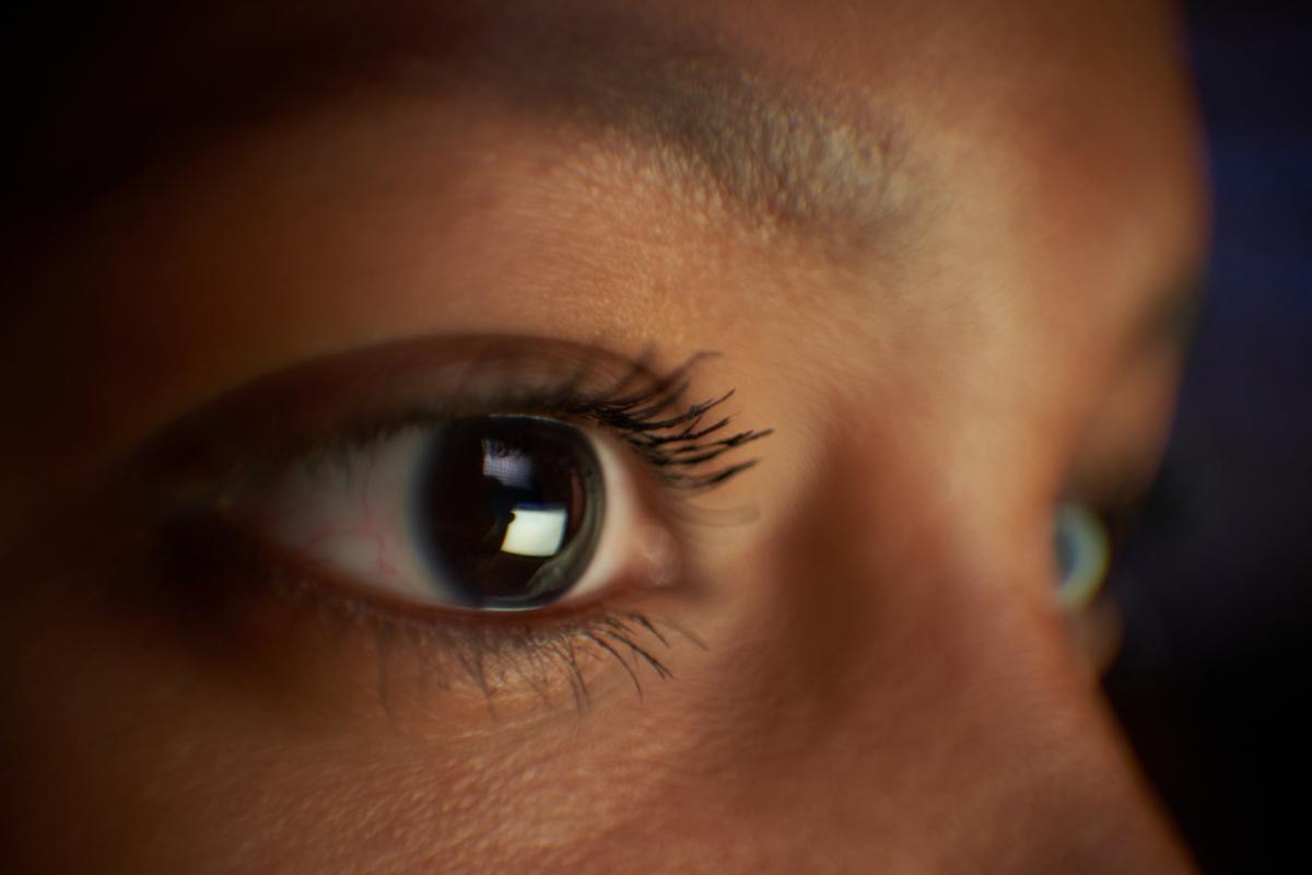Primer plano de la mirada de una mujer afroamericana mirando la pantalla de un ordenador portátil por la noche, trabajando hasta tarde.