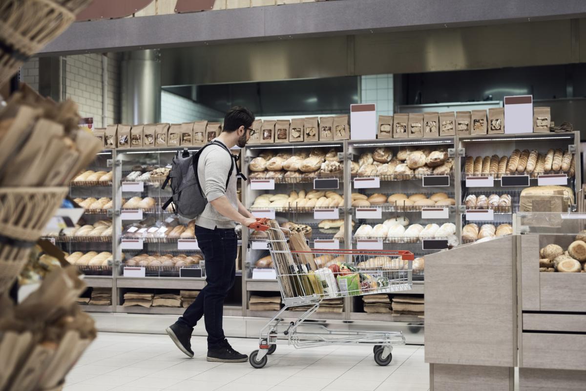 un hombre caminando con un carrito mientras mira la sección de panadería en el supermercado.