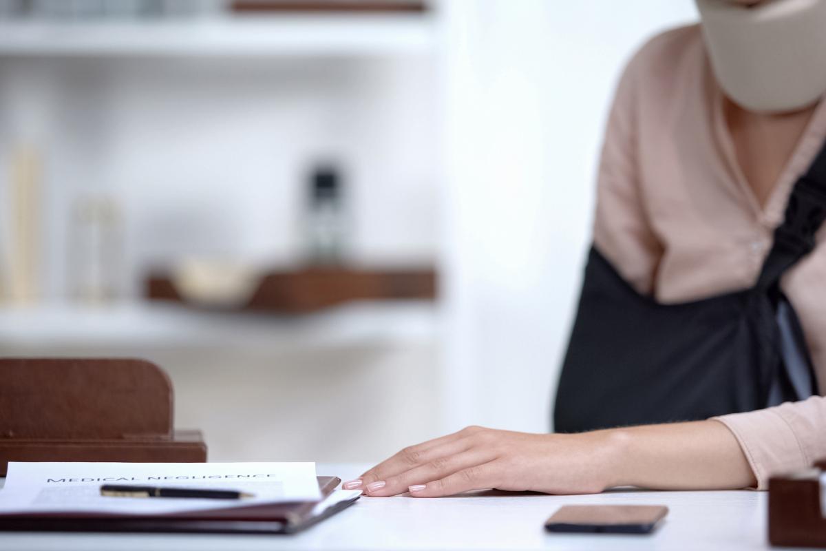 Una chica con el brazo escayolado y collarín delante de un papel que confirma su baja médica.