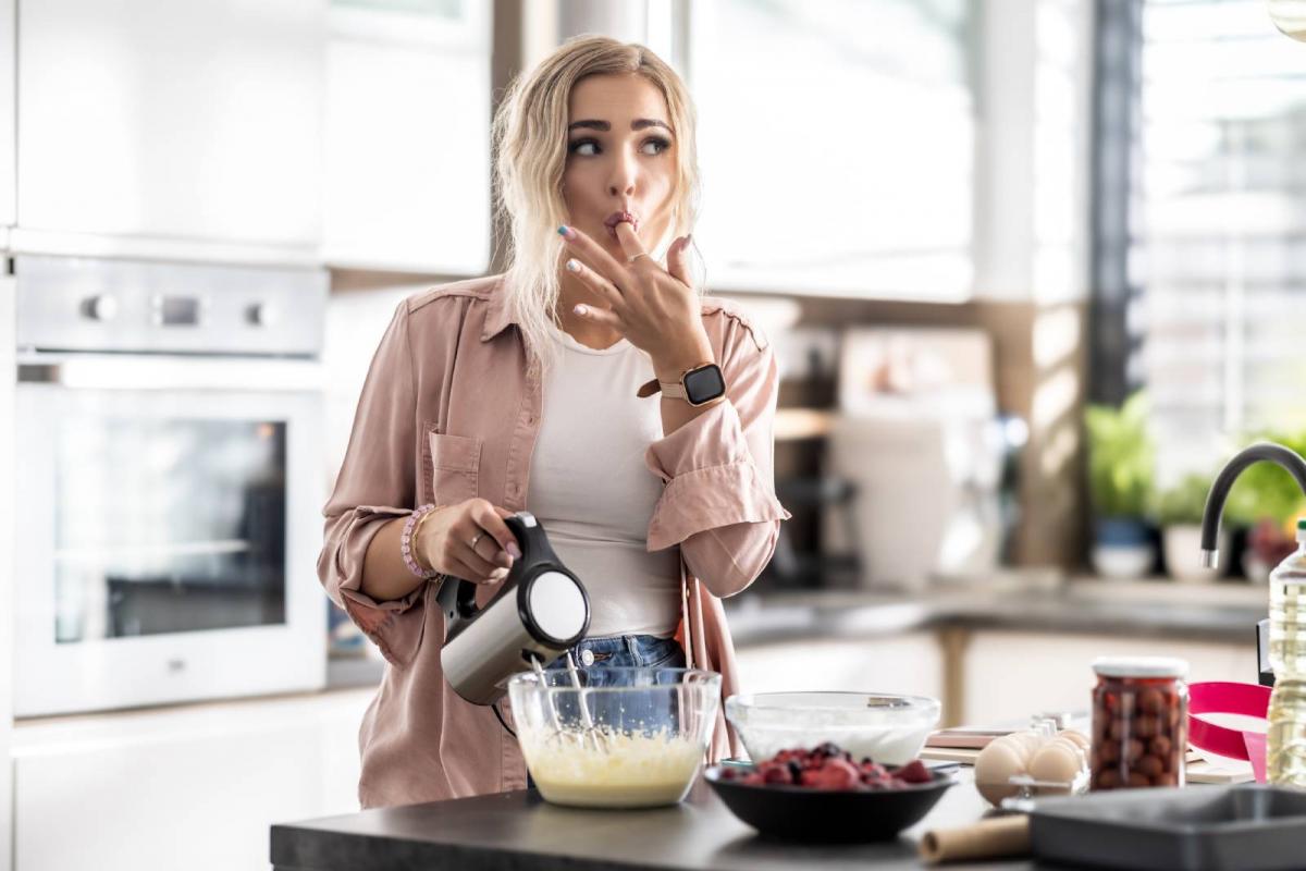 Joven mezclando masa para pastel y chupándose los dedos para probarla