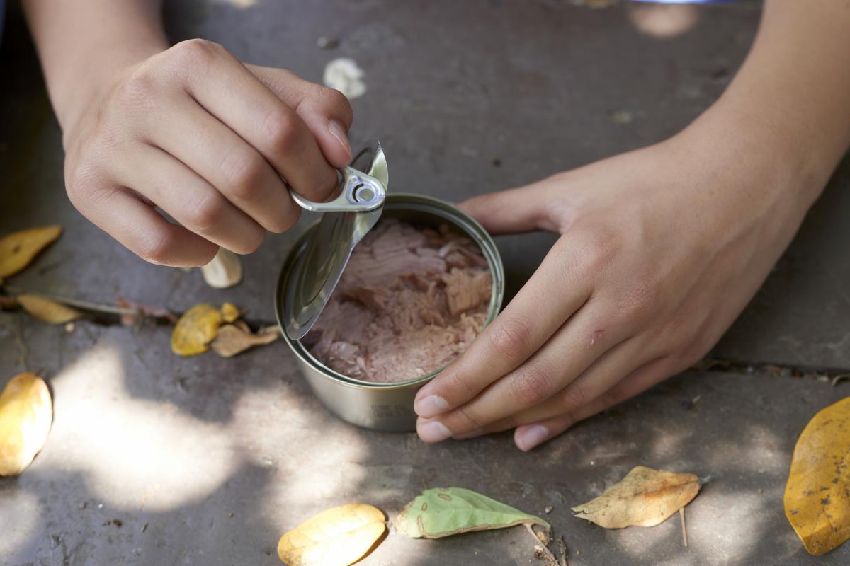 Un adolescente abren una lata de atún mientras disfruta de una excursión de senderismo.
