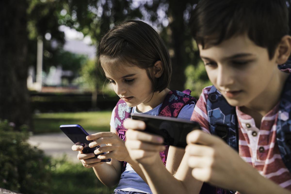 Un niño y una niña con un móvil cada uno mientras están en el parque.