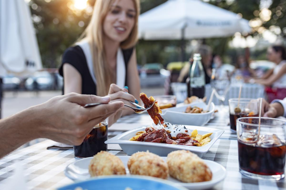 Clientes probando croquetas y patatas bravas en un bar.