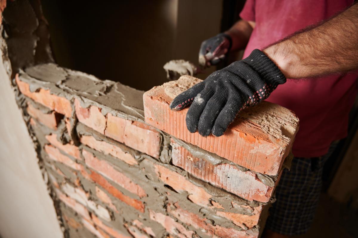Trabajador albañil construyendo una pared de ladrillo en el sitio de construcción