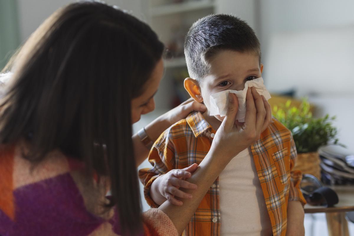 Mujer ayuda a niño a sonarse.