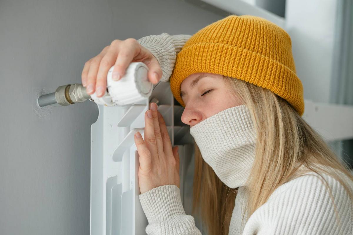 Mujer con sombrero calentándose mientras está sentada en el suelo cerca del radiador