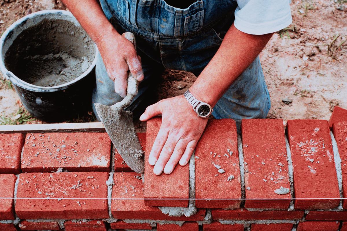 Manos de un albañil mientras coloca un ladrillo en un área de construcción.
