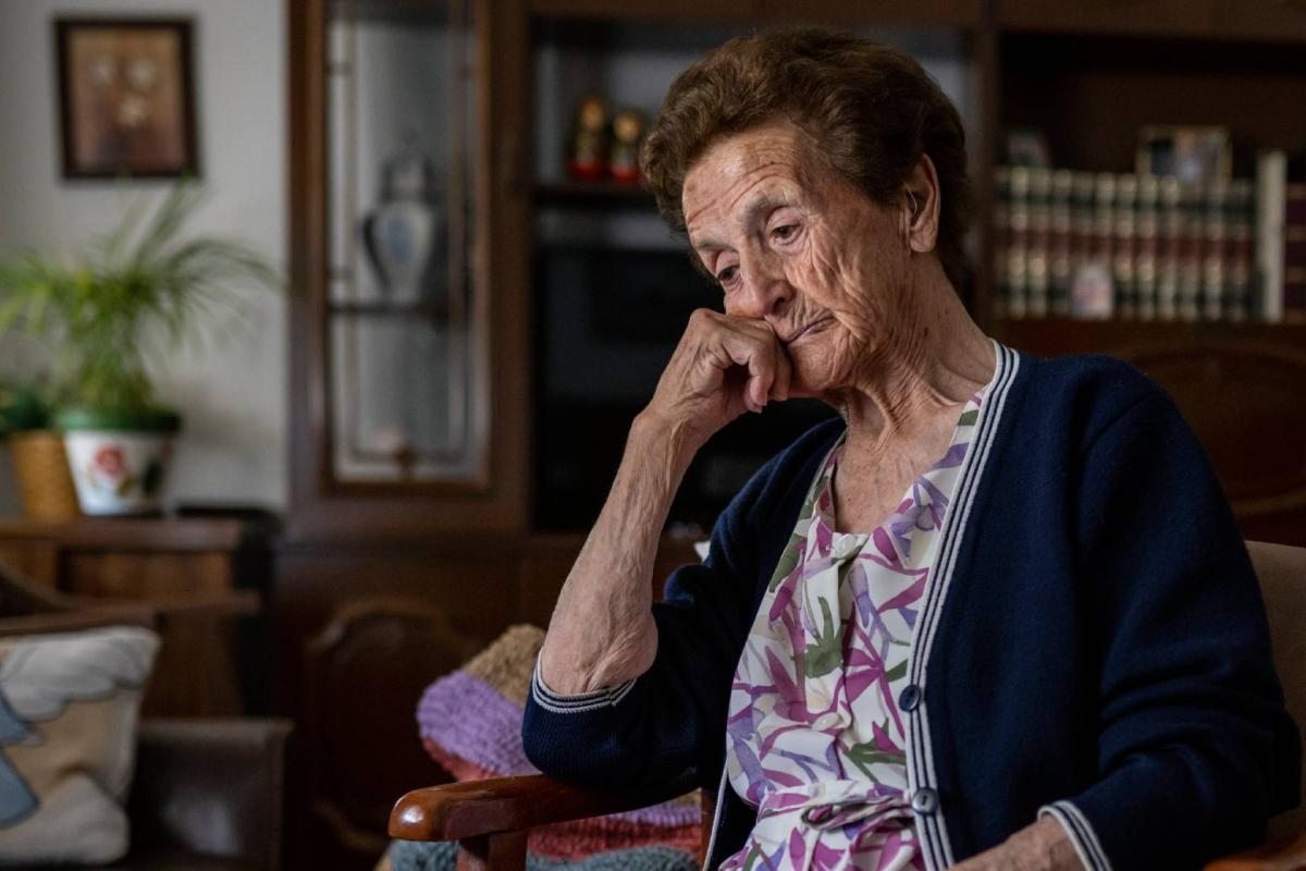 Mujer mayor sentada sola en el sofá, con gesto triste, pensando en sus problemas, recordando momentos de su vida, echando de menos a sus hijos y sintiendo soledad