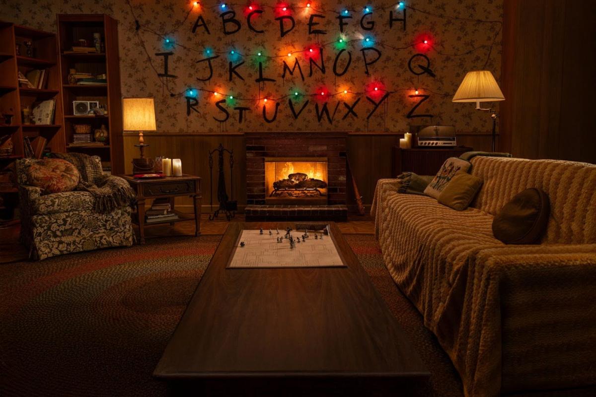 Salón de los Byers de Stranger Things con la pared del alfabeto iluminada y la chimenea encendida.