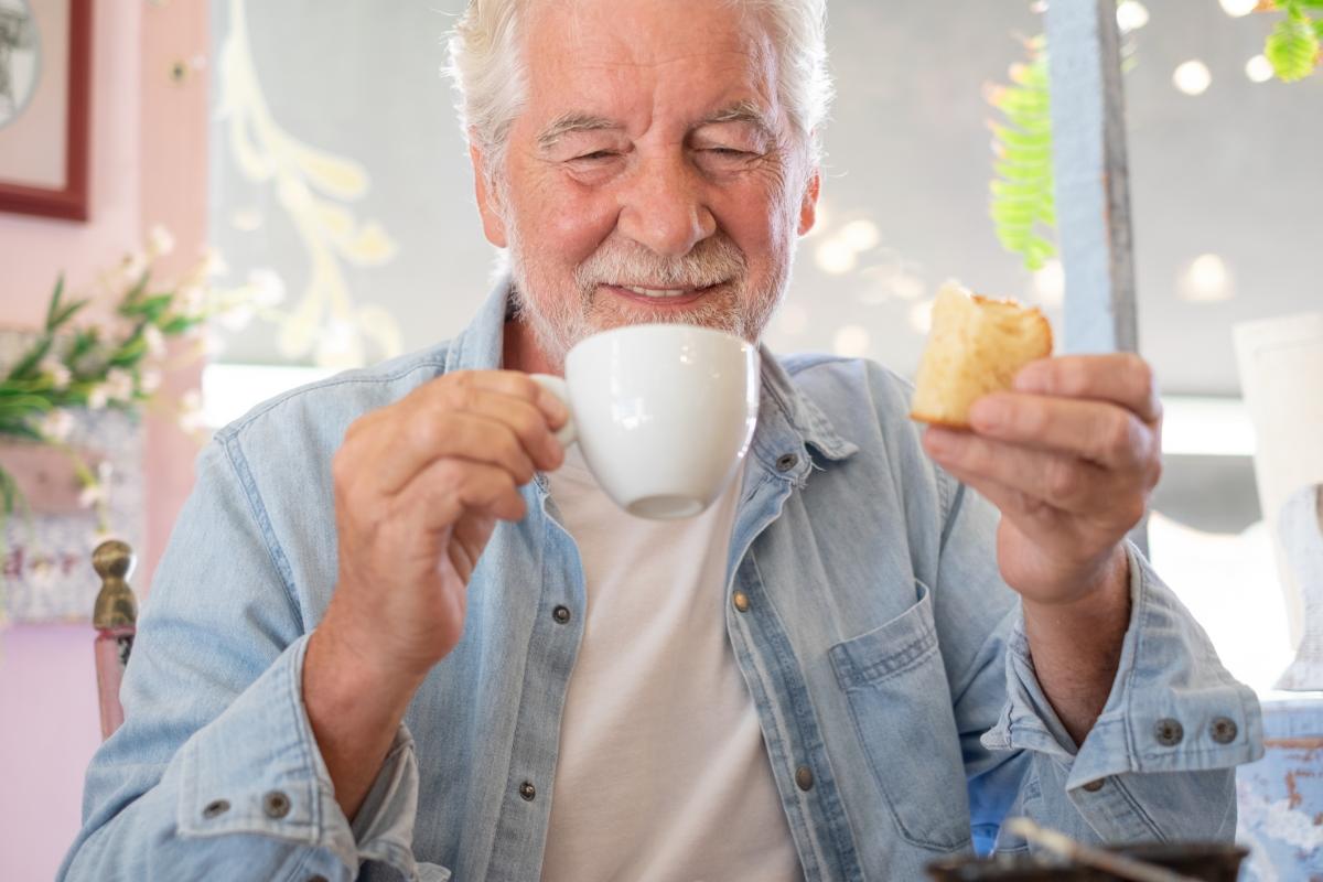 Un hombre mayor en una cafetería desayunando capuchino y dulces. Personas mayores sonrientes disfrutando de su jubilación y una vida libre.