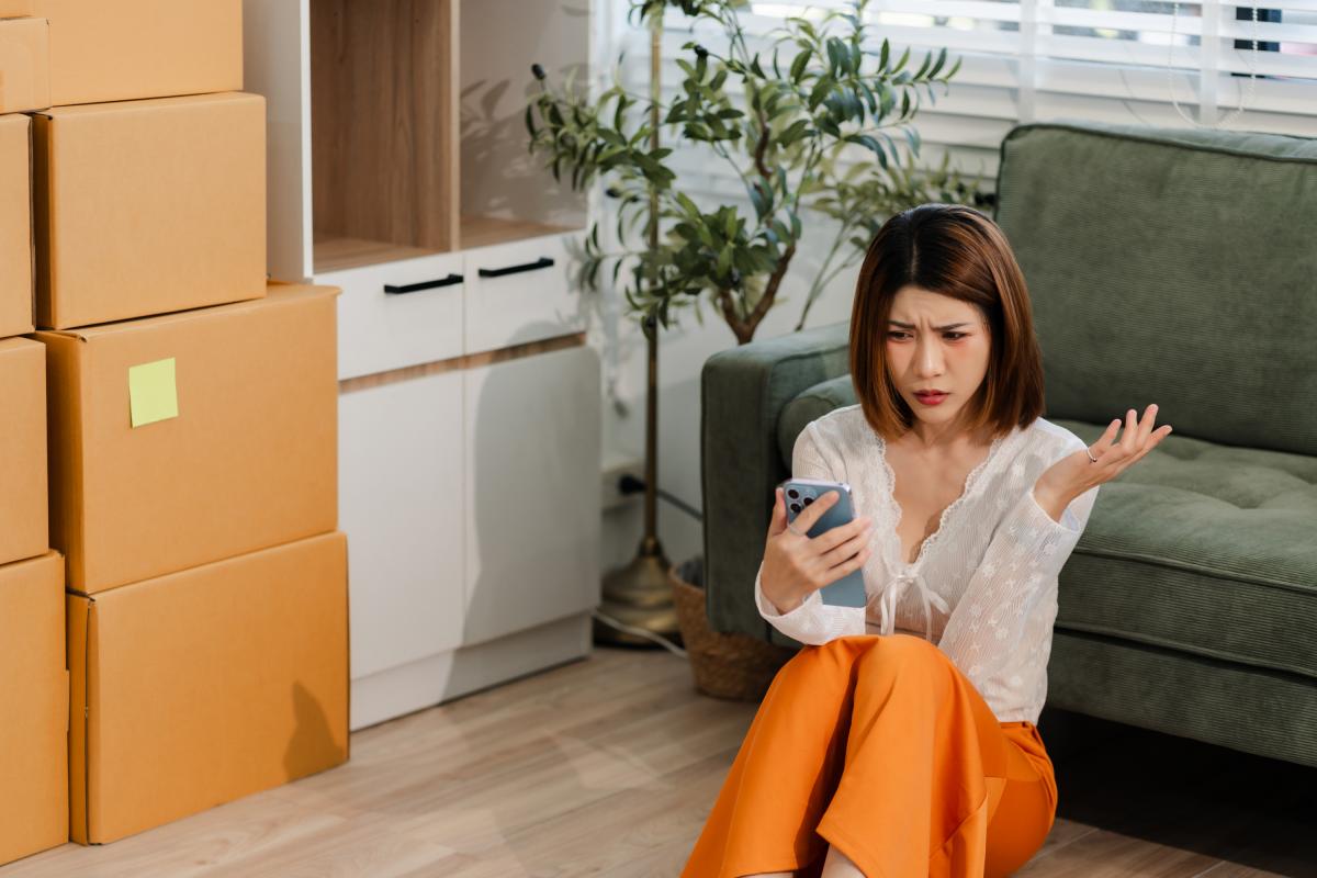 Una mujer mira el móvil con cara de enfado mientras realiza una mudanza