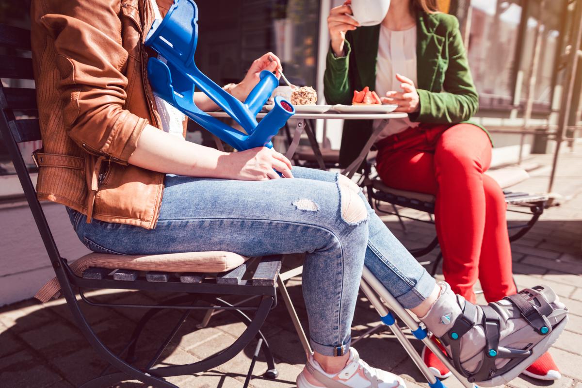 Dos mujeres, una con una pierna rota y muletas, en un café tomando café y pastel.