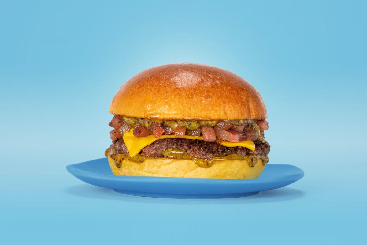 Hamburguesa con queso cheddar derretido, trocitos de bacon y salsa verde sobre un pan brioche en un plato azul