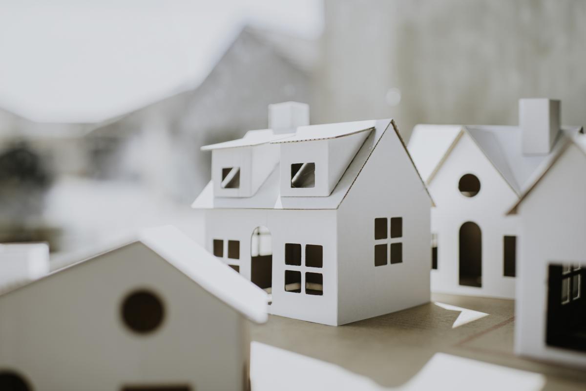 Imagen conceptual y sencilla de casas de cartón, blancas, lisas, de diversas formas y tamaños, con espacio para copiar.