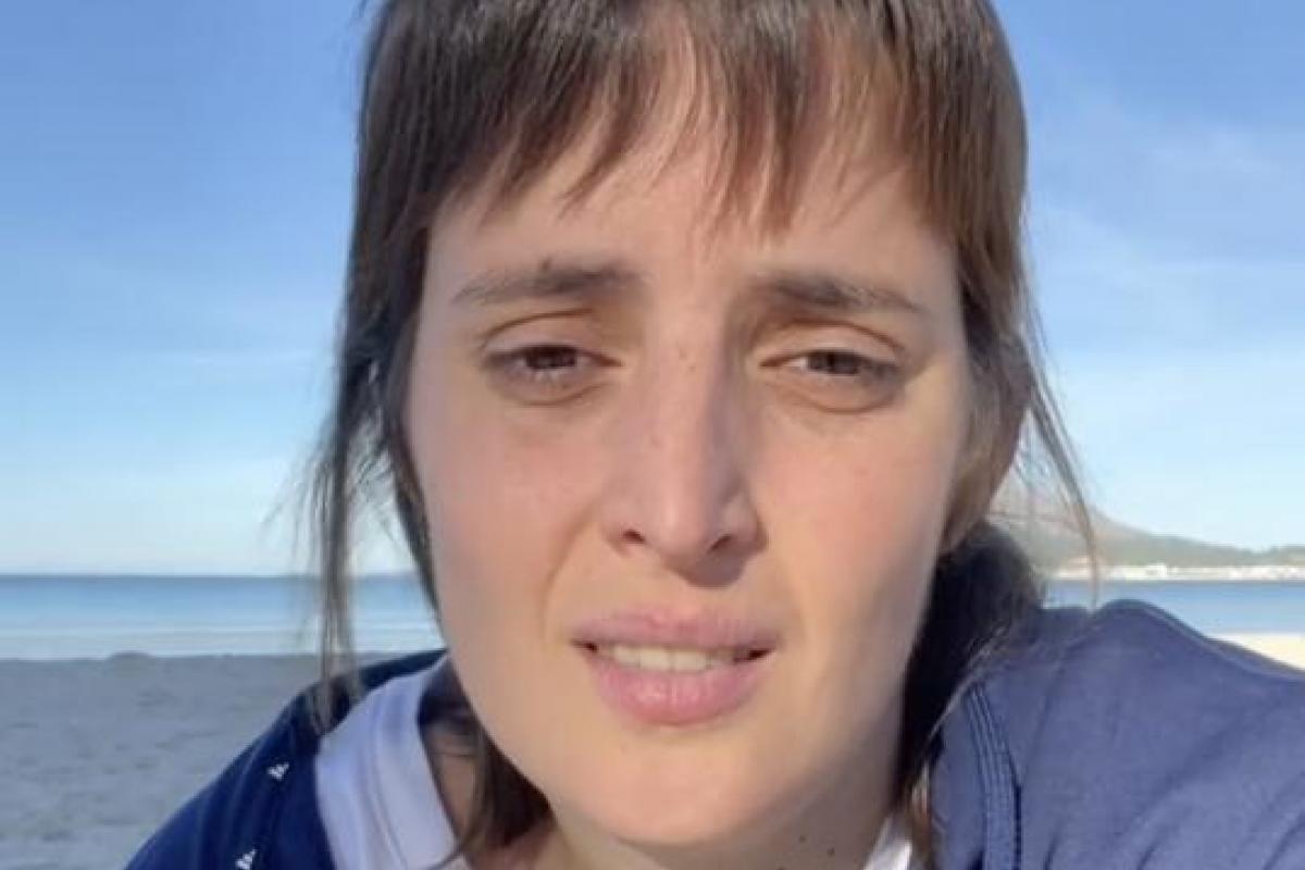 Captura de Florencia Conforti sentada en la arena hablando a cámara con el mar al fondo.