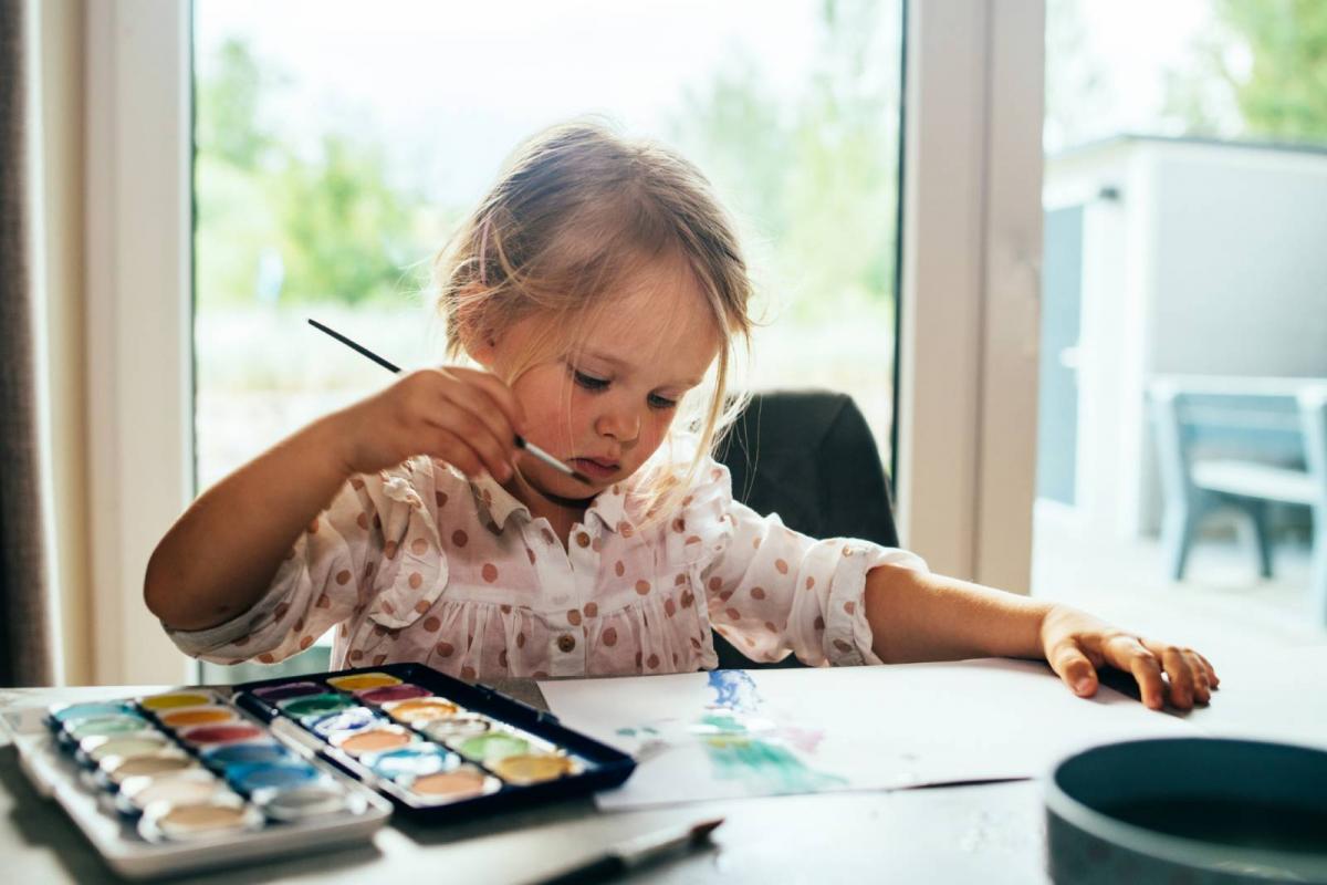 Niña pequeña pintando con acuarelas en casa