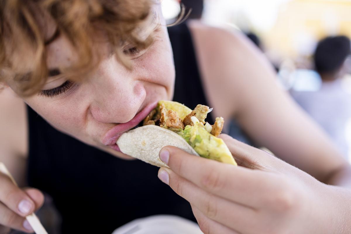 Joven comiendo un taco con las manos en un entorno urbano.