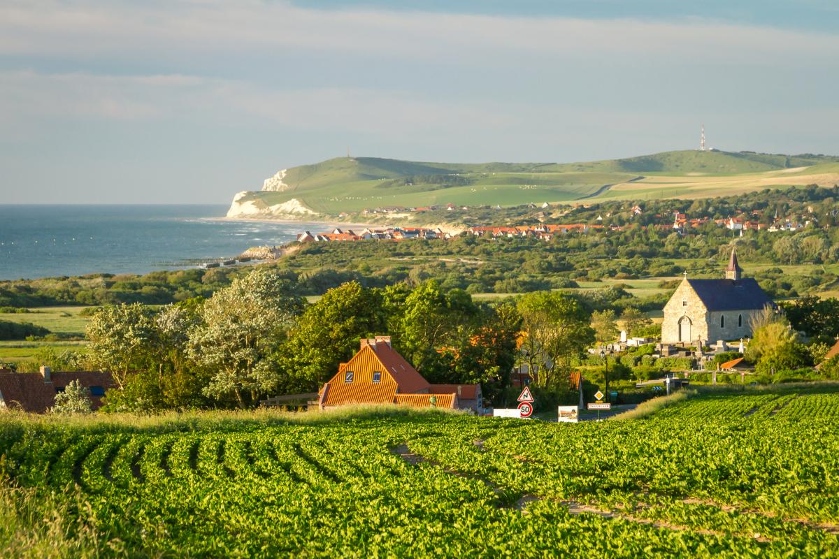 Vista de una zona agrícola en el norte de Francia, con cultivos, viviendas rurales y la costa al fondo en un día despejado.