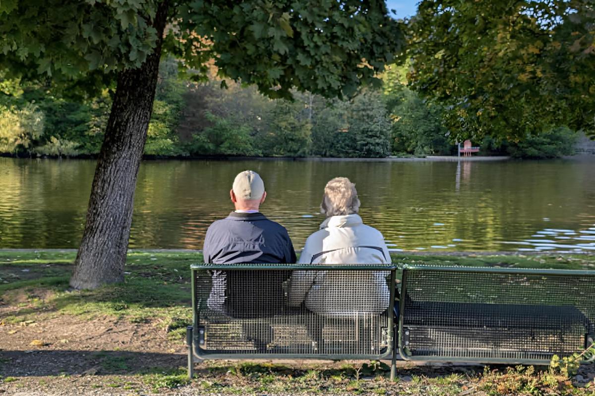 Una pareja de jubilados sentados de espalda de cara a un lago