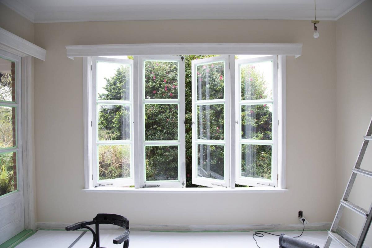 Interior de una habitación recién pintada con una ventana abierta, una escalera y herramientas de reforma