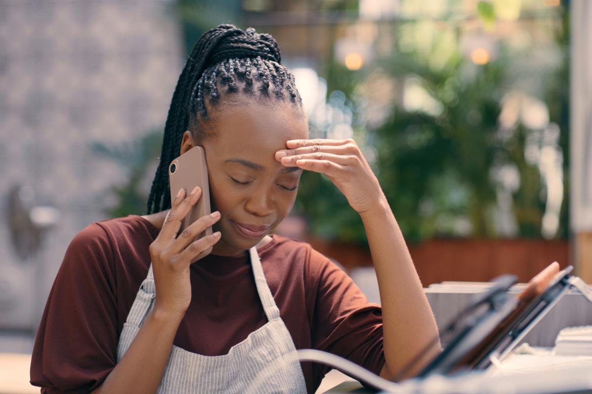 Café, llamada telefónica y mujer negra llorando con estrés, dolor de cabeza o desastre, riesgo o noticias. Camarera africana con conversación a través de un teléfono inteligente, agotamiento o crisis de salud mental