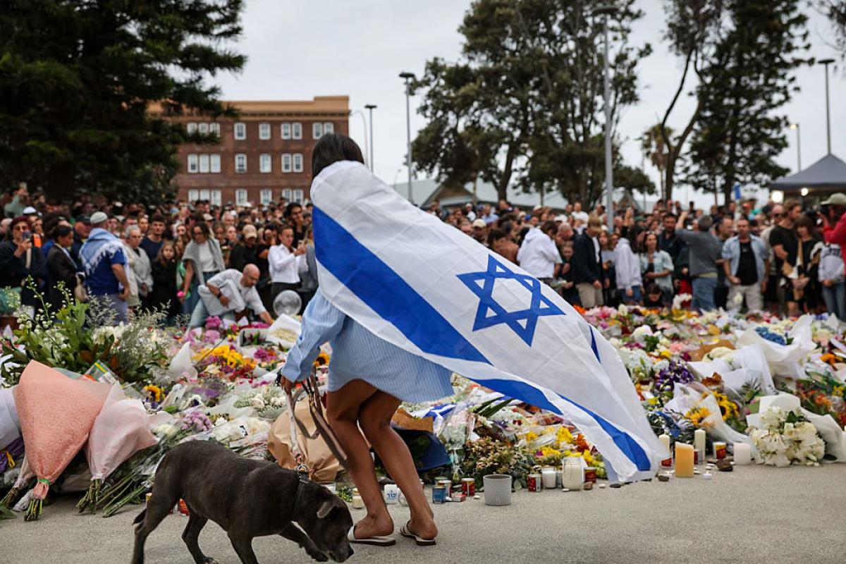 Una persona de luto con una bandera israelí deposita flores en Bondi Beach.
