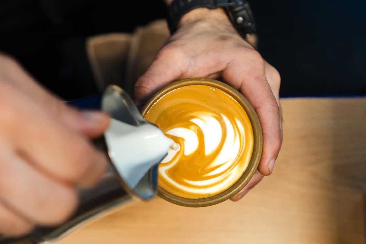 Un barista sirviendo un café con un dibujo en la espuma.