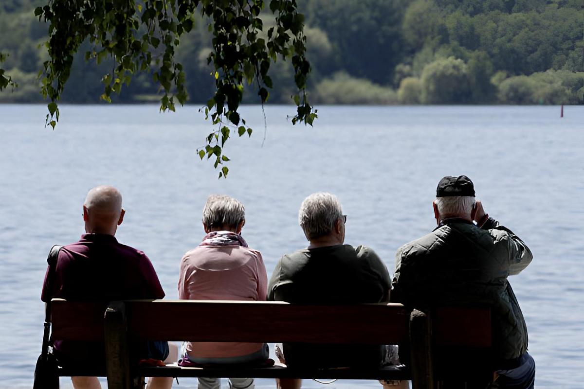 Un grupo de personas mayores sentadas en un banco frente a un lago
