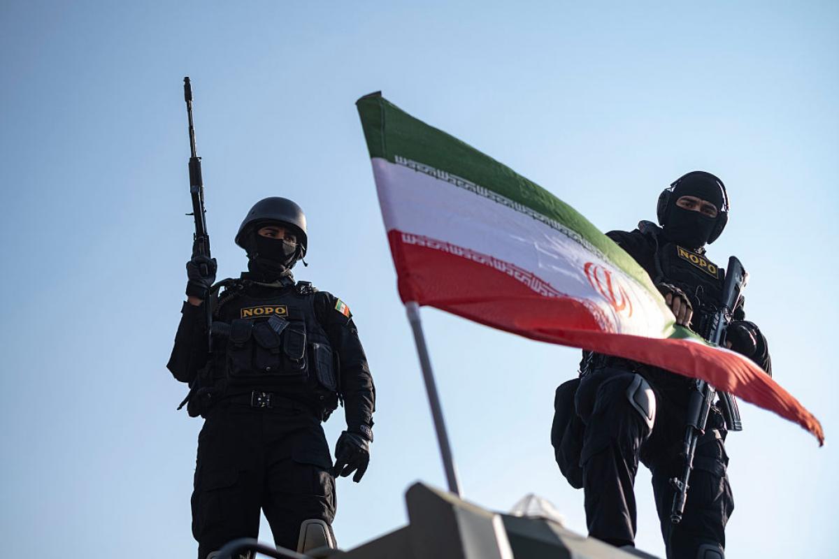 Dos miembros armados de las fuerzas especiales de la policía iraní, tras una bandera iraní colocada en un blindado, durante una manifestación progubernamental en el centro de Teherán, el 12 de enero de 2026.