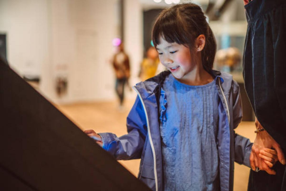 Lovely cheerful girl checking out exhibits with interactive touch screen in art gallery.
