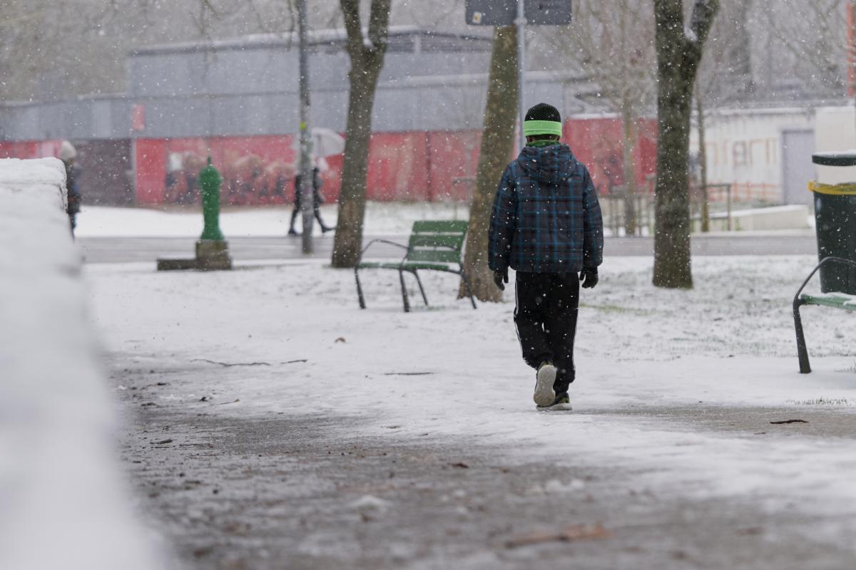 Vista trasera de un niño con ropa de invierno caminando por las calles de la ciudad en un día nevado.