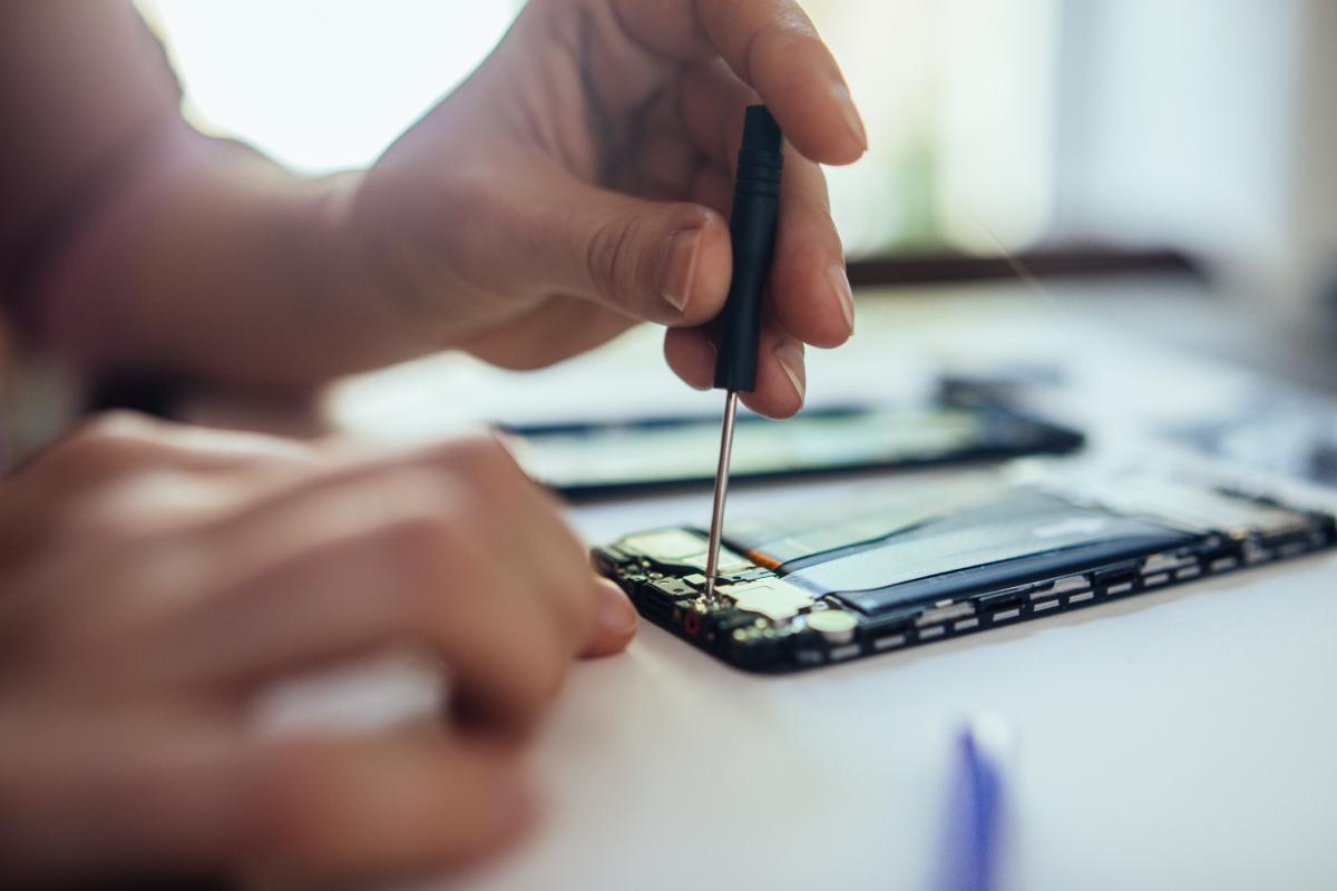 Reparación de celulares en casa. Mujer reparando un celular en casa, cambiando una pieza dañada.